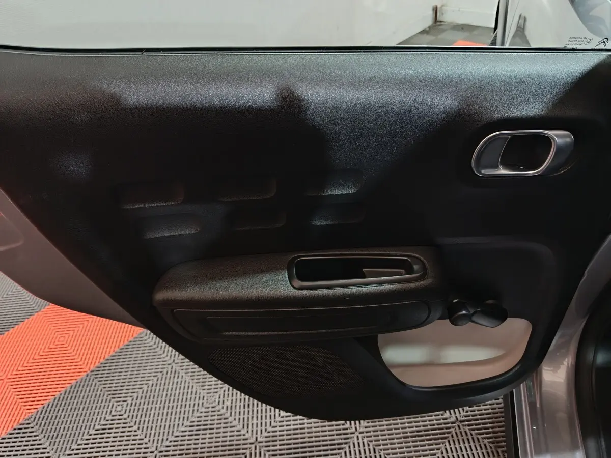 Vue intérieure de la porte côté droit d'une Citroën C3 gris clair, avec poignée et manivelle de vitre manuelle.