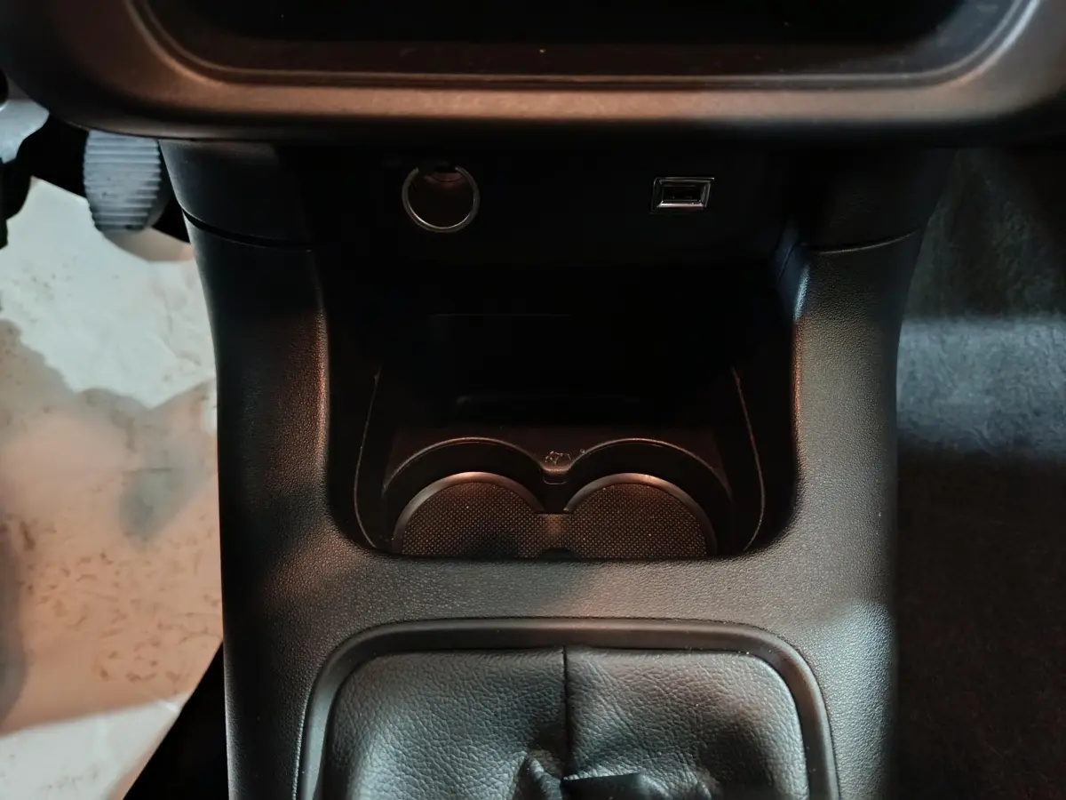 Vue rapprochée de la console centrale noire avec porte-gobelets, prise 12V et port USB sur Citroën C3 gris clair 2024.