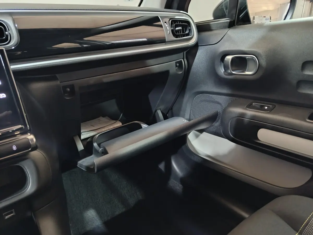 Intérieur de la Citroën C3 2024 gris clair, vue côté passager avec boîte à gants ouverte et tableau de bord noir brillant.