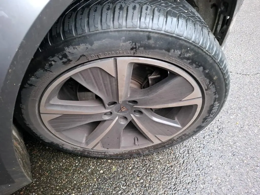 Gros plan sur la jante alu gris foncé avec logo CUPRA au centre, montée sur un pneu noir humide.