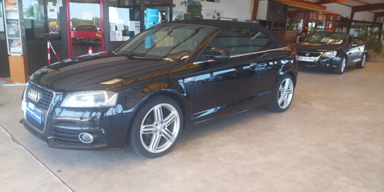 Audi A3 Cabriolet noir vue 3/4 avant droit avec capote fermée, jantes alliage et intérieur sombre en showroom.