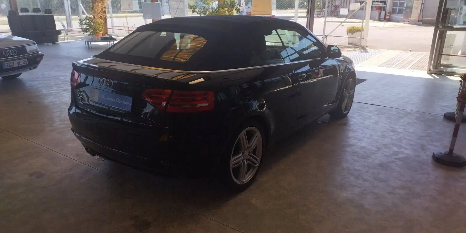 Audi A3 Cabriolet noir vue 3/4 arrière droit, capote fermée, jantes alliage et feux arrière allumés.