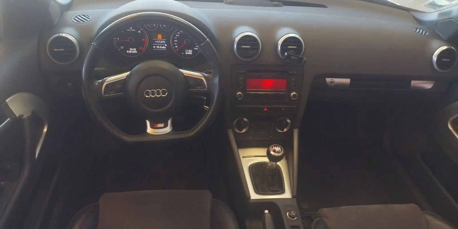 Vue intérieure de l'Audi A3 Cabriolet 2010 noir, tableau de bord et volant sport avec levier de vitesse manuel visible.