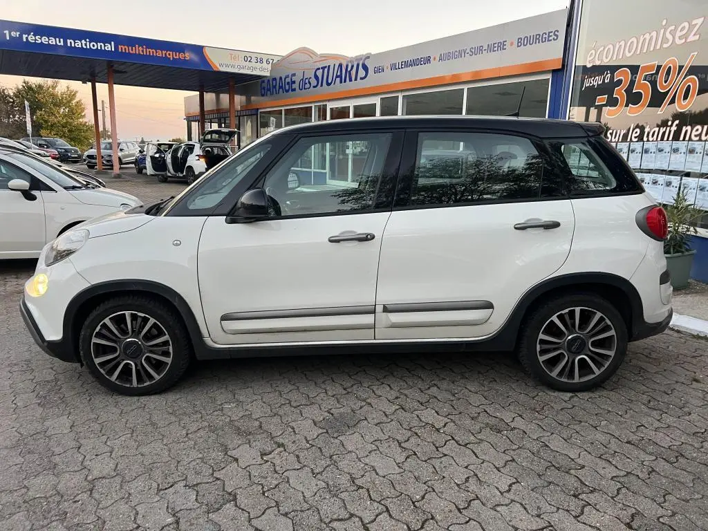Vue de profil côté gauche d'une Fiat 500L Lounge 2017 bi-color avec toit noir, stationnée devant un garage multimarques.