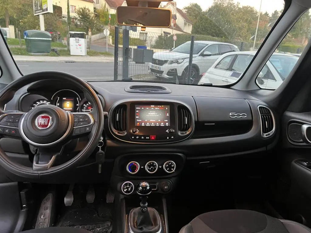 Vue intérieure avant du tableau de bord noir de la Fiat 500L avec volant multifonction et écran tactile central.
