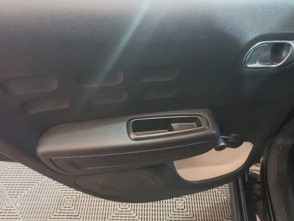 Gros plan sur la porte intérieure côté droit de la Citroën C3 noire, avec poignée et commande de vitre manuelle.