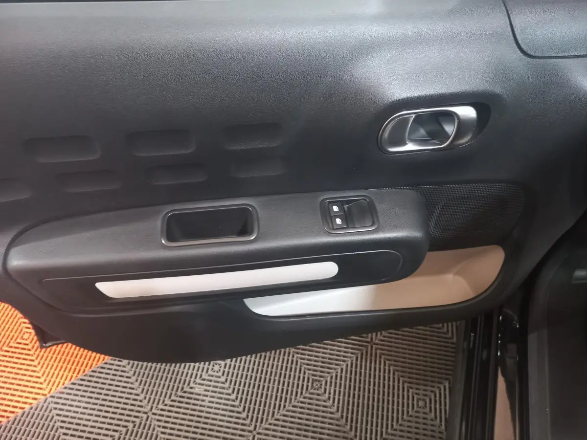 Vue rapprochée de la porte intérieure côté conducteur de la Citroën C3 noire, avec poignée argentée et commandes de vitres.