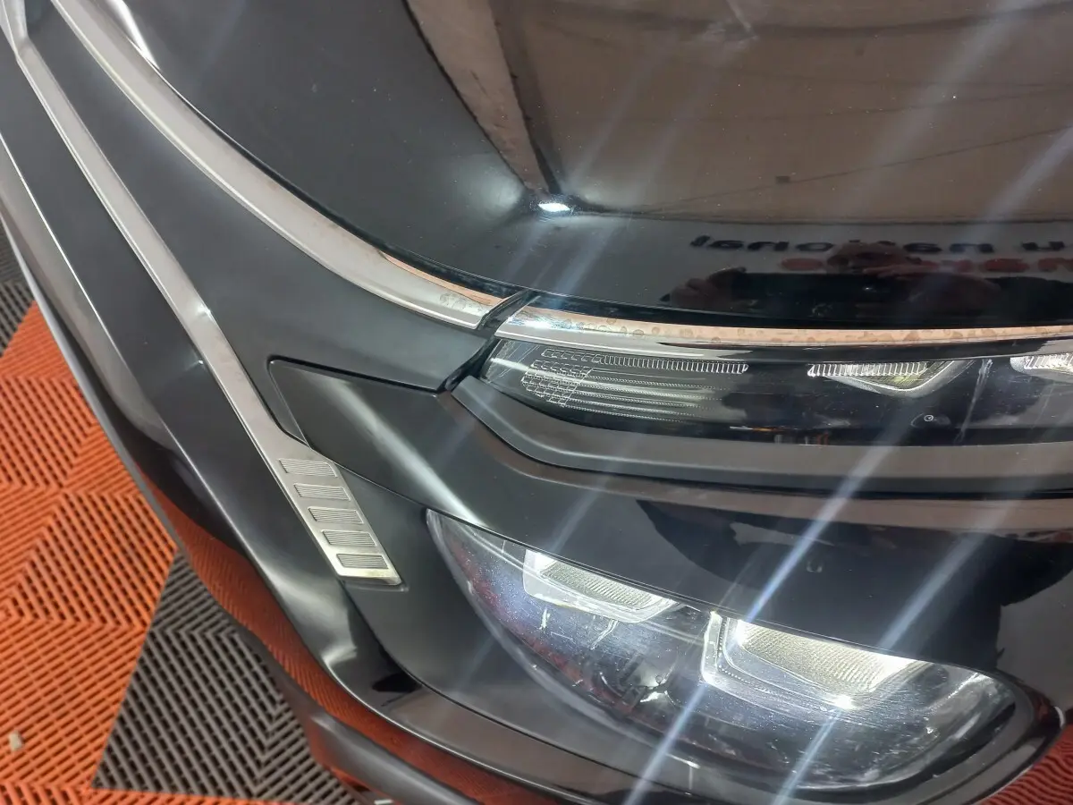 Gros plan sur le phare avant gauche noir brillant de la Citroën C3 2024 avec détails chromés et LED allumées.