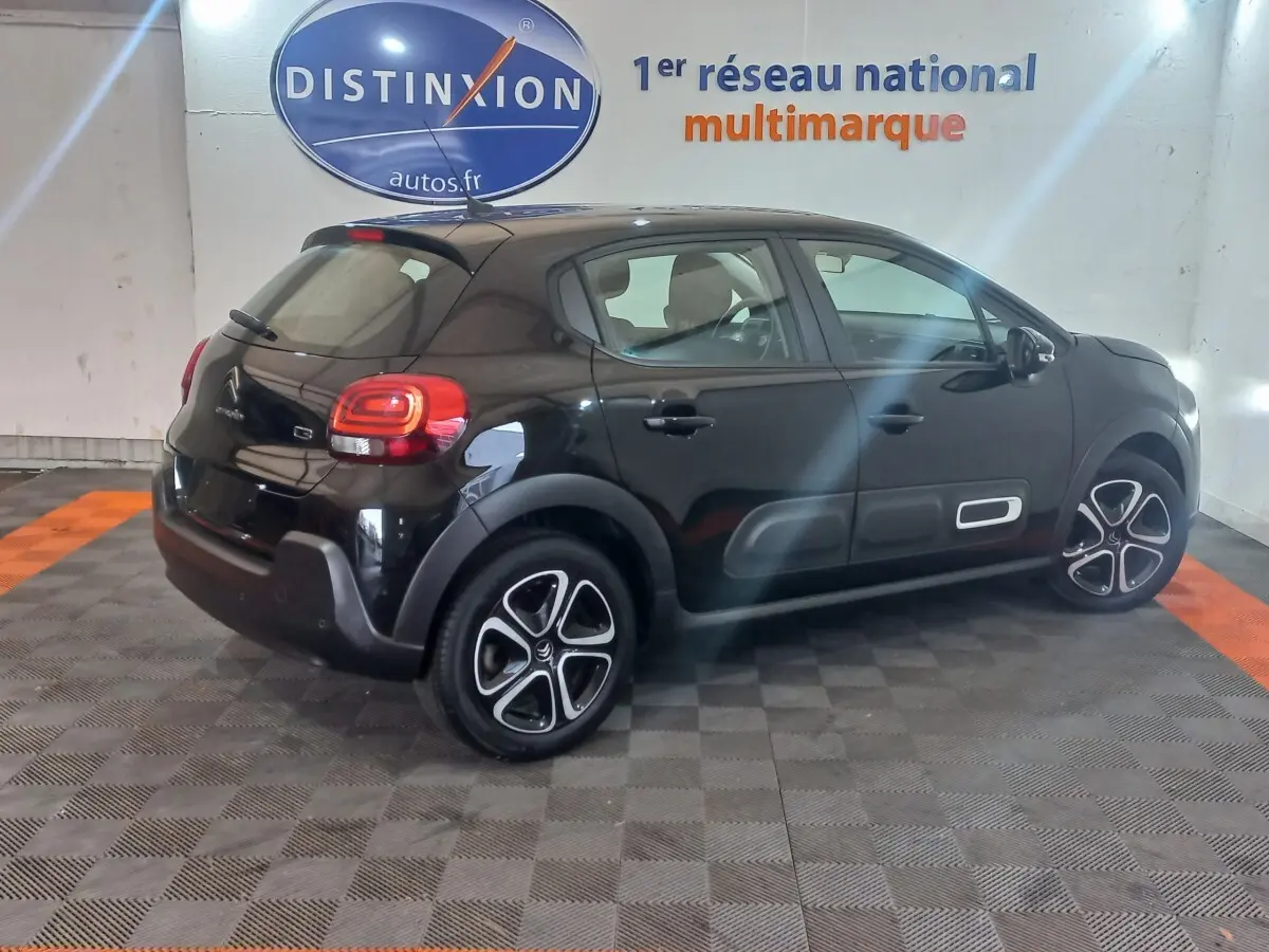 Vue 3/4 arrière droite d'une Citroën C3 noire 2024 avec protections latérales blanches et jantes stylisées.
