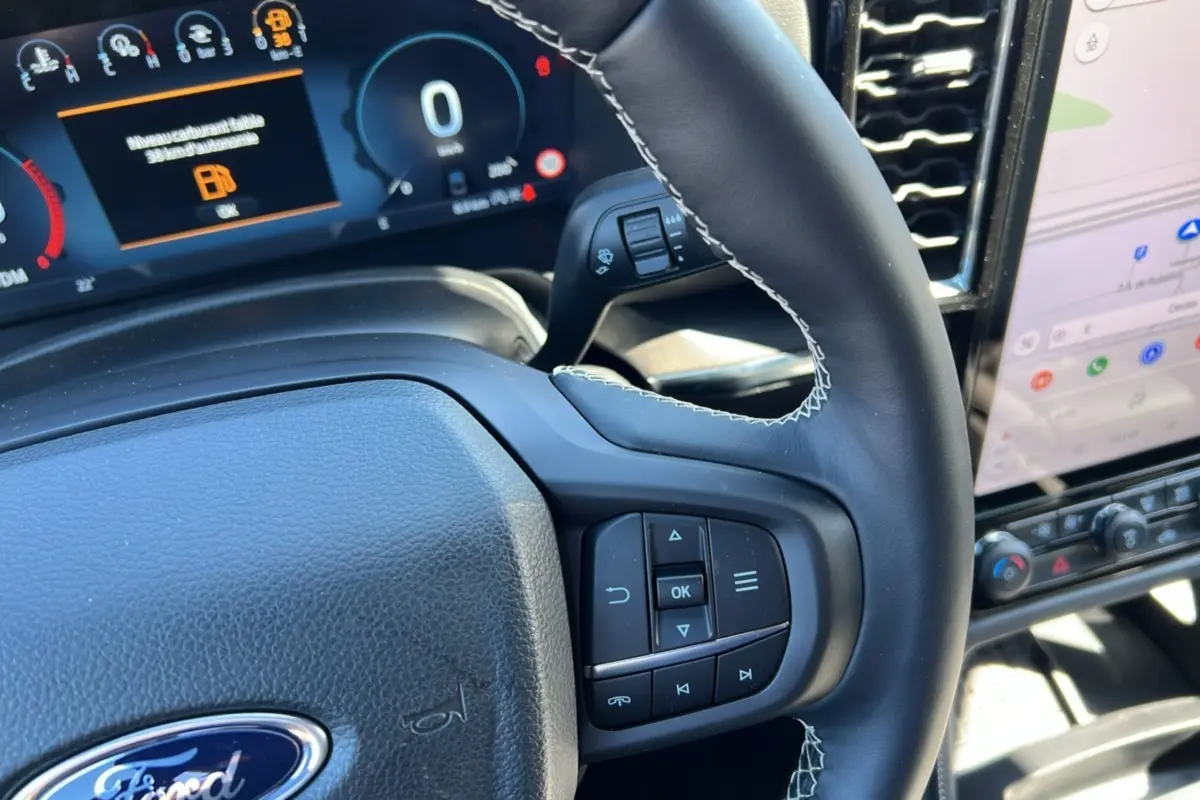 Gros plan sur le volant cuir noir avec commandes multifonctions du Ford Ranger 2026, tableau de bord numérique en arrière-plan.