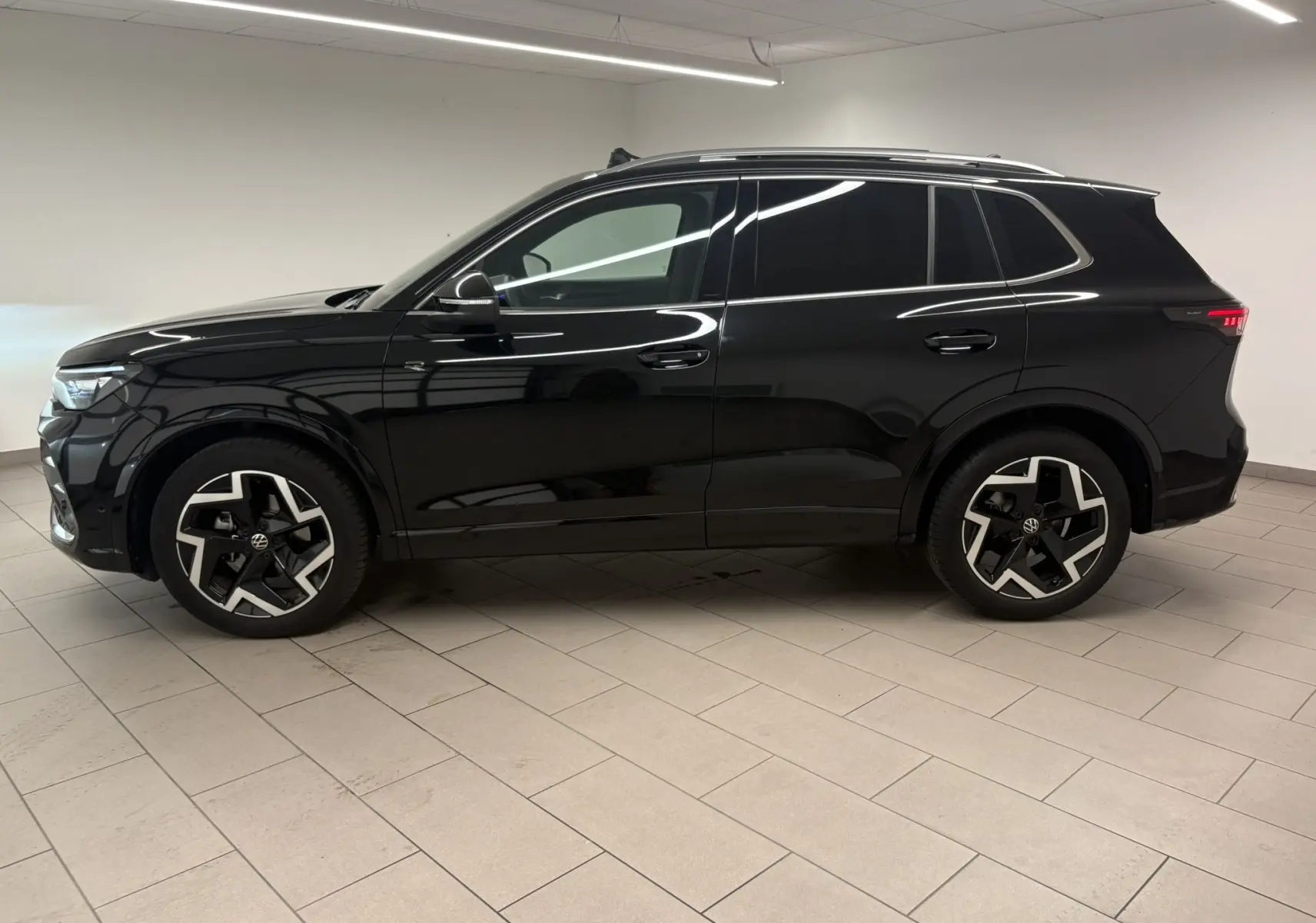 Vue de profil côté gauche du Volkswagen Tiguan 2025 noir intense nacré avec jantes R-Line distinctives en intérieur neutre.