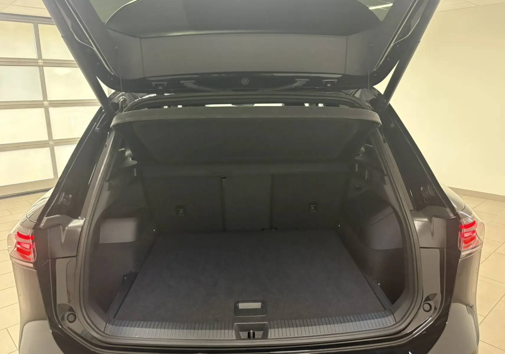 Coffre ouvert vu de l'arrière d'un Volkswagen Tiguan 2025 noir intense nacré avec hayon et intérieur de coffre spacieux.