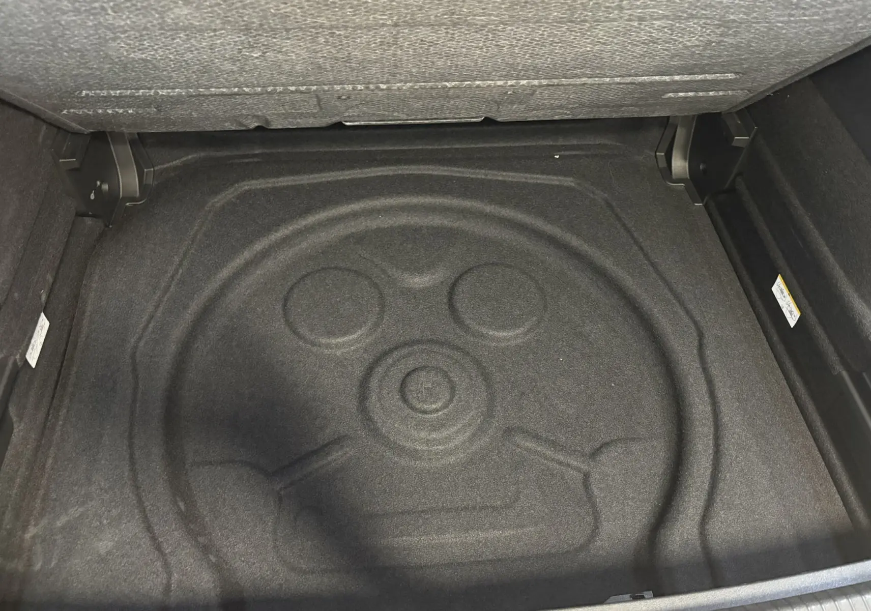 Coffre ouvert du Volkswagen Tiguan 2025, vue plongeante sur l’espace de rangement avec tapis de sol noir.