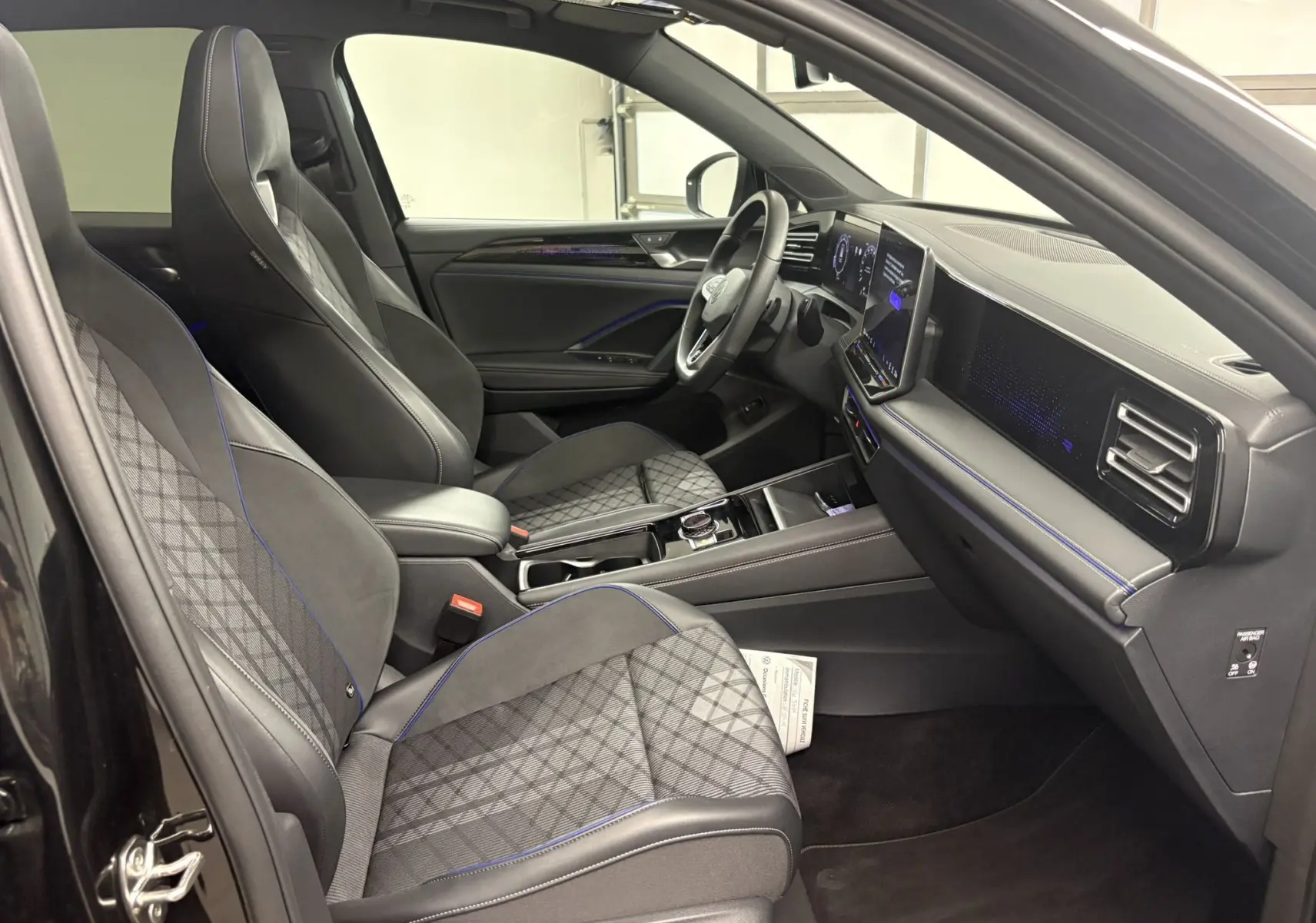 Vue intérieure côté conducteur du Volkswagen Tiguan 2025 noir intense nacré, sièges sport avec surpiqûres bleues et tableau de bord digital.