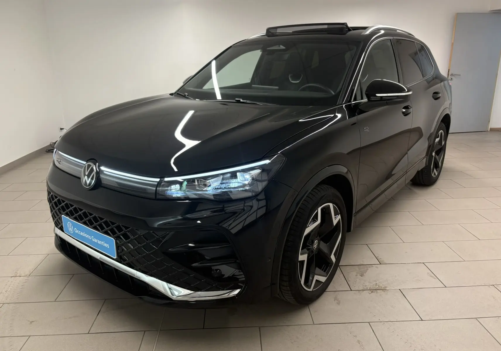 Vue 3/4 avant droite du Volkswagen Tiguan 2025 noir intense nacré avec jantes R-Line et toit ouvrant visible.