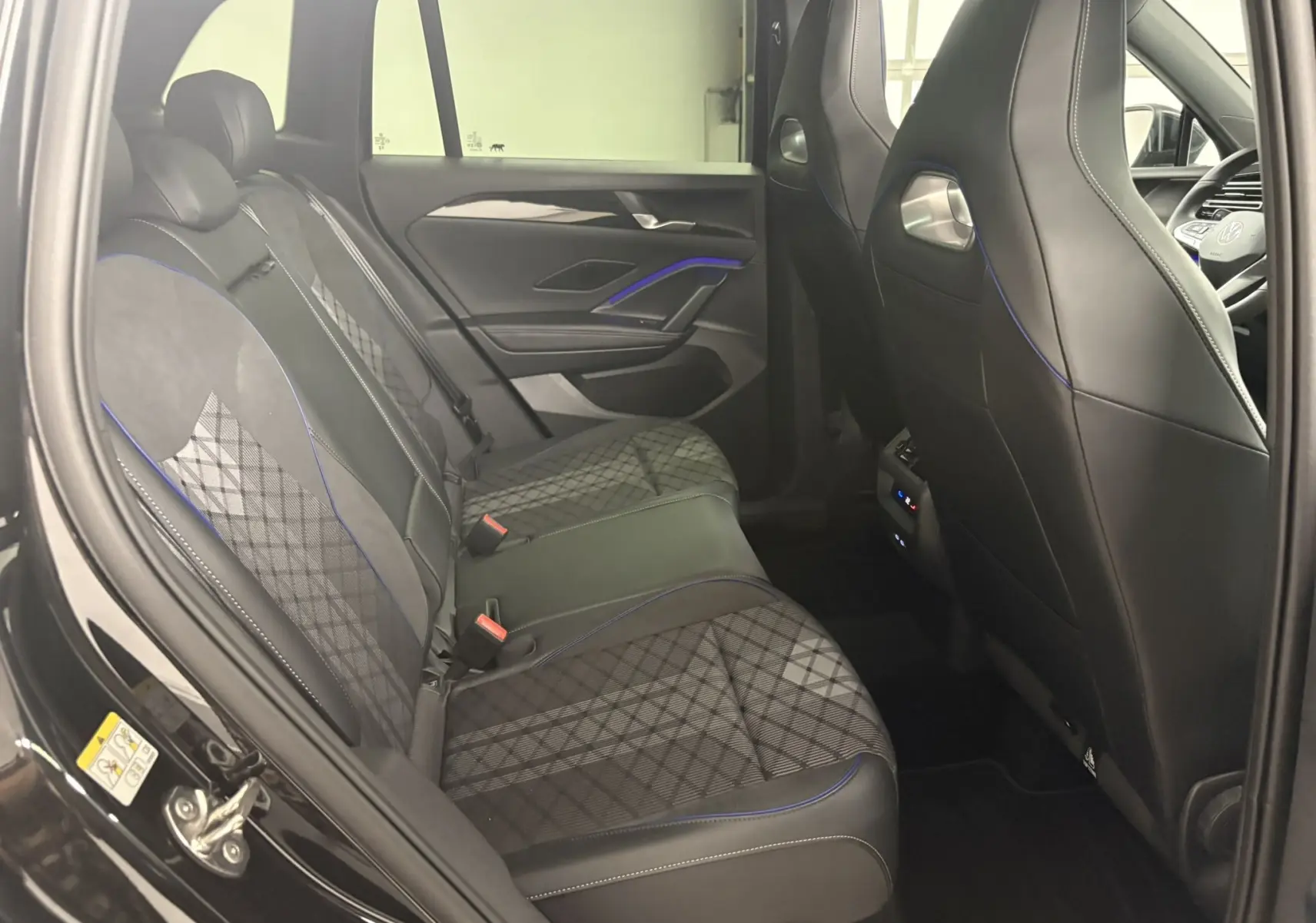 Vue intérieure arrière côté gauche du Volkswagen Tiguan 2025 avec sièges en tissu noir à motifs et surpiqûres bleues.