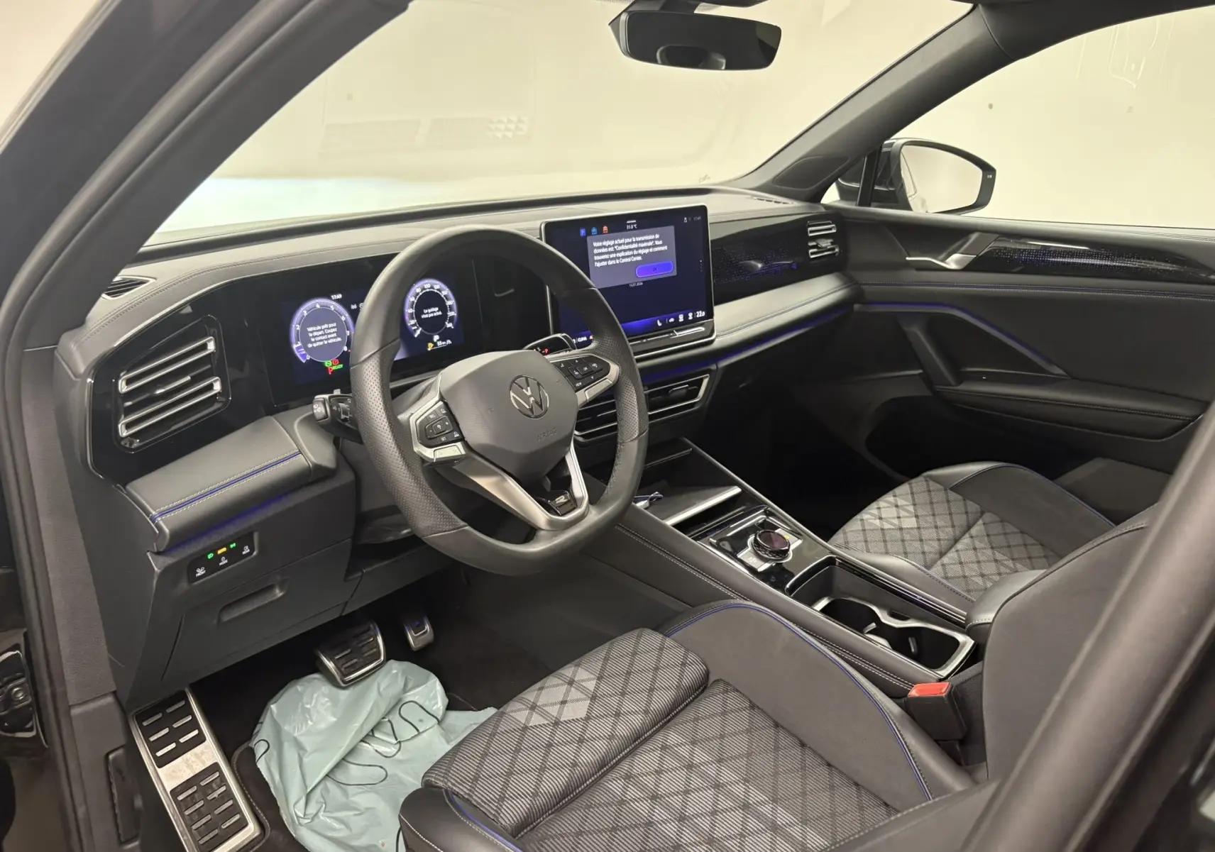 Vue intérieure côté conducteur du Volkswagen Tiguan 2025 avec tableau de bord numérique et sellerie cuir noire à surpiqûres bleues.