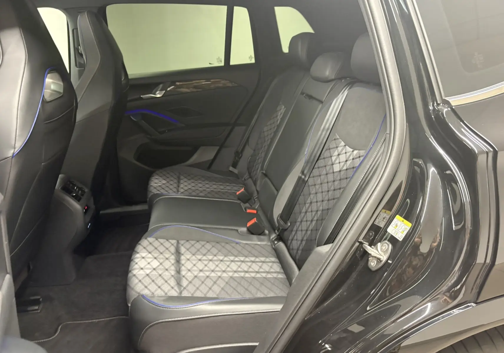 Vue côté droit de l'intérieur arrière du Volkswagen Tiguan 2025 noir intense nacré avec sièges en cuir et tissu à surpiqûres bleues.