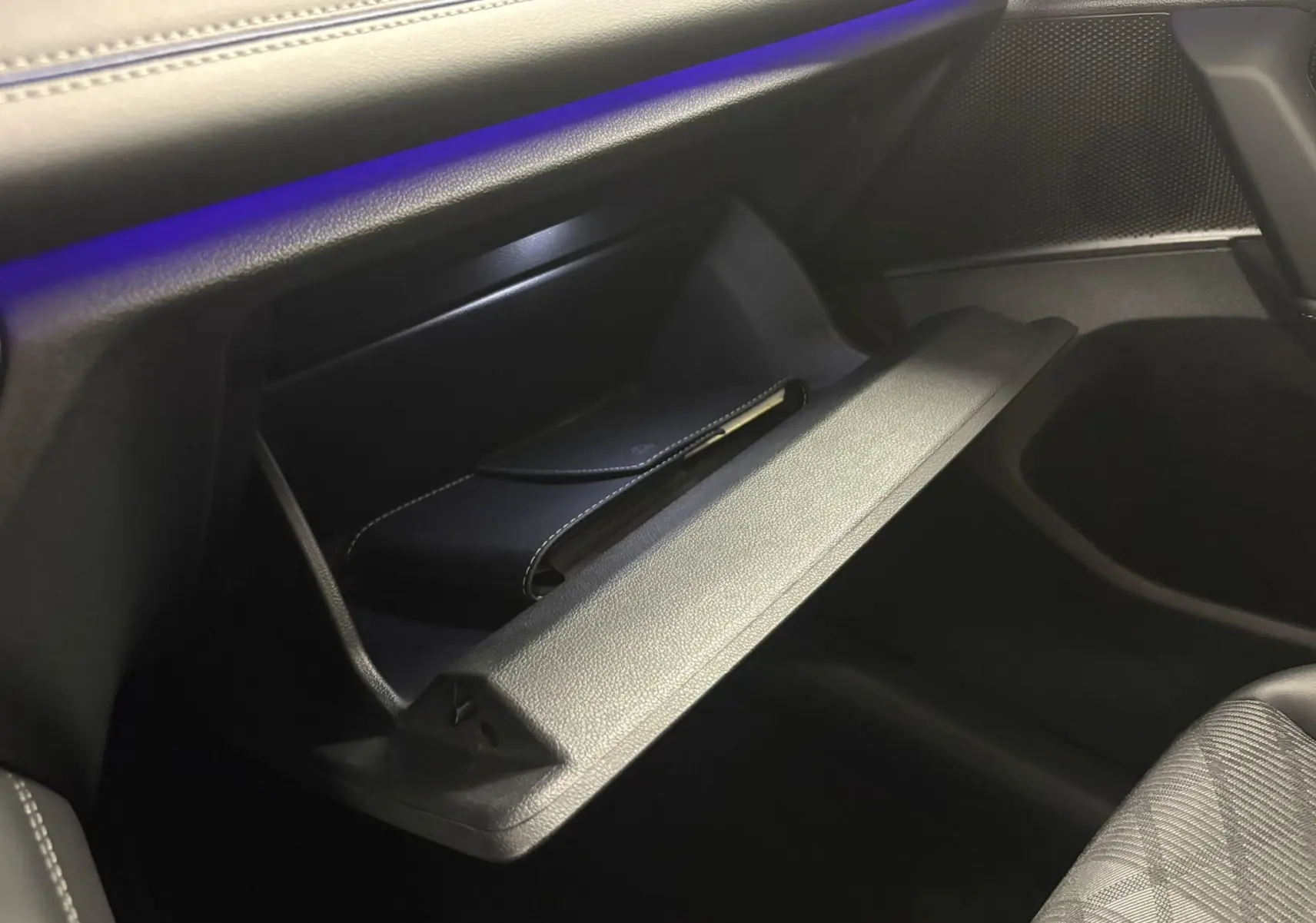 Gros plan sur la boîte à gants ouverte côté passager du Volkswagen Tiguan 2025, intérieur noir avec éclairage bleu subtil.