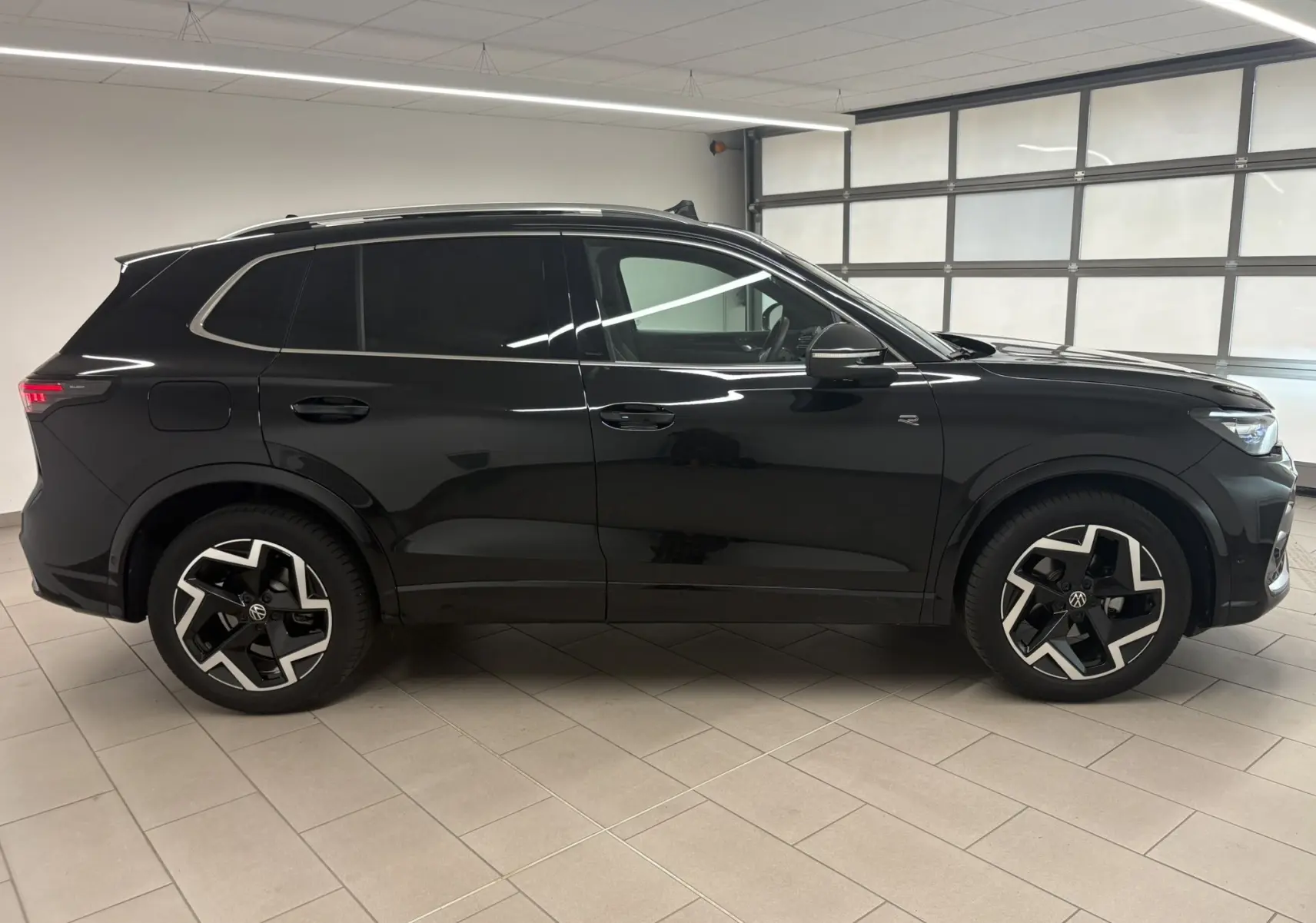 Profil droit du Volkswagen Tiguan 2025 noir intense nacré avec jantes R-Line distinctives et toit ouvrant visible.