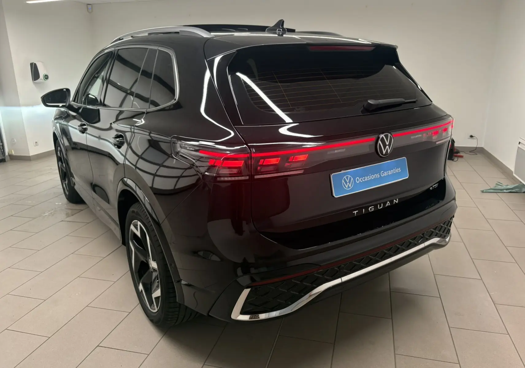 Vue 3/4 arrière gauche du Volkswagen Tiguan 2025 noir intense nacré avec feux arrière LED et toit ouvrant en intérieur showroom.