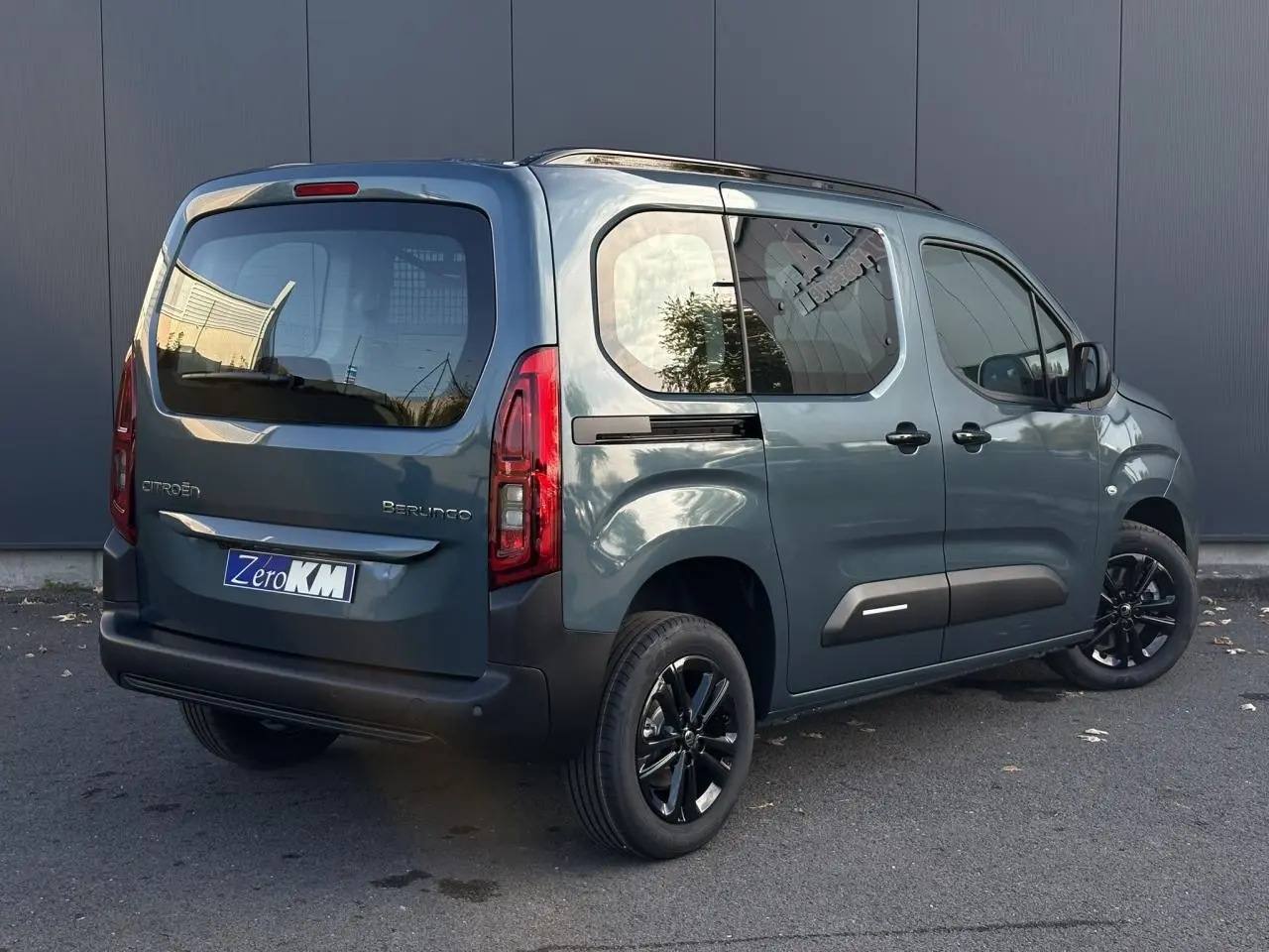 Vue 3/4 arrière droite d'un Citroën Berlingo Multispace bleu métallisé avec jantes alliage noires et barres de toit.