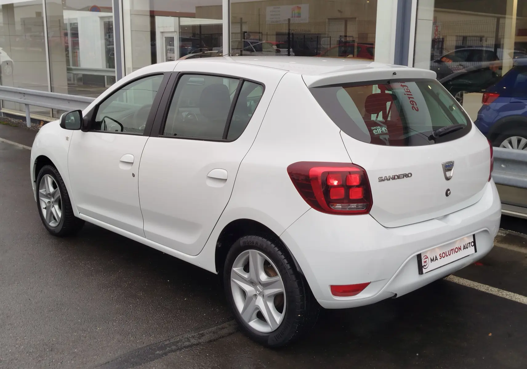 Vue 3/4 arrière droite d'une Dacia Sandero blanc glacier de 2019 avec feux arrière LED et cinq portes.