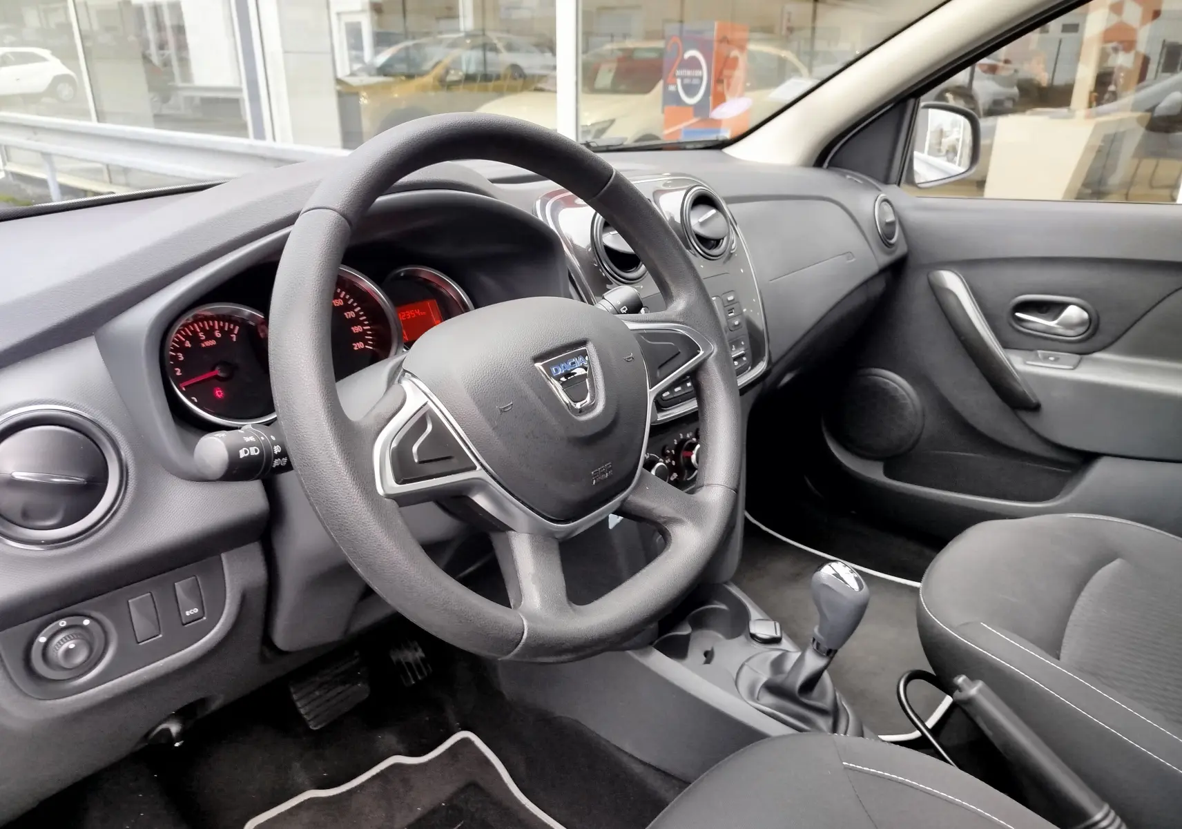 Vue intérieure côté conducteur du tableau de bord et volant noir de la Dacia Sandero 2019 avec sellerie tissu gris.
