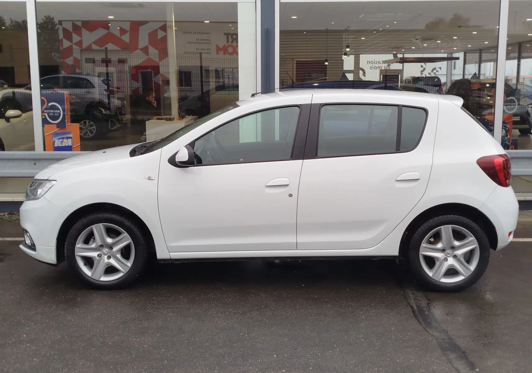Profil côté gauche d'une Dacia Sandero blanc glacier de 2019, version Lauréate Easy-R, garée devant une vitrine.