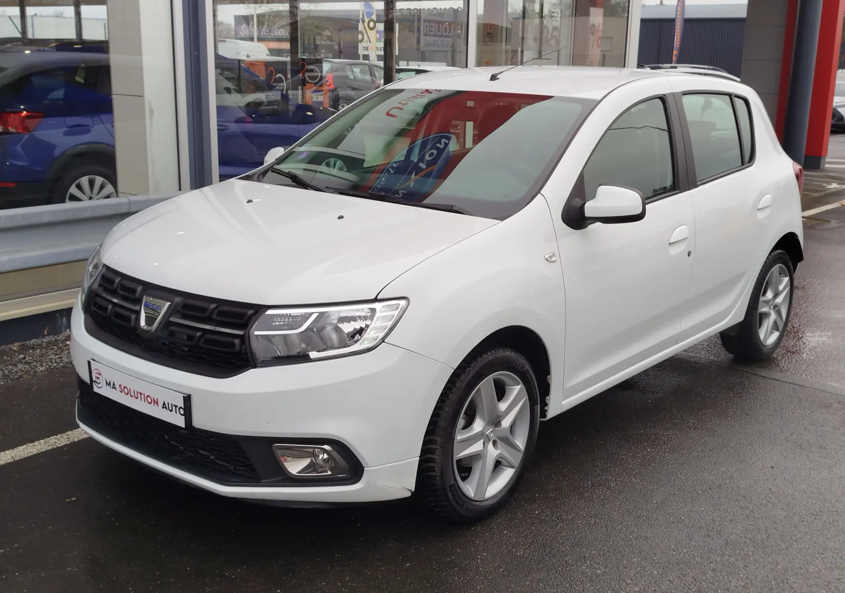 Dacia Sandero blanc glacier vue 3/4 avant droit, avec calandre noire et jantes alliage cinq branches.