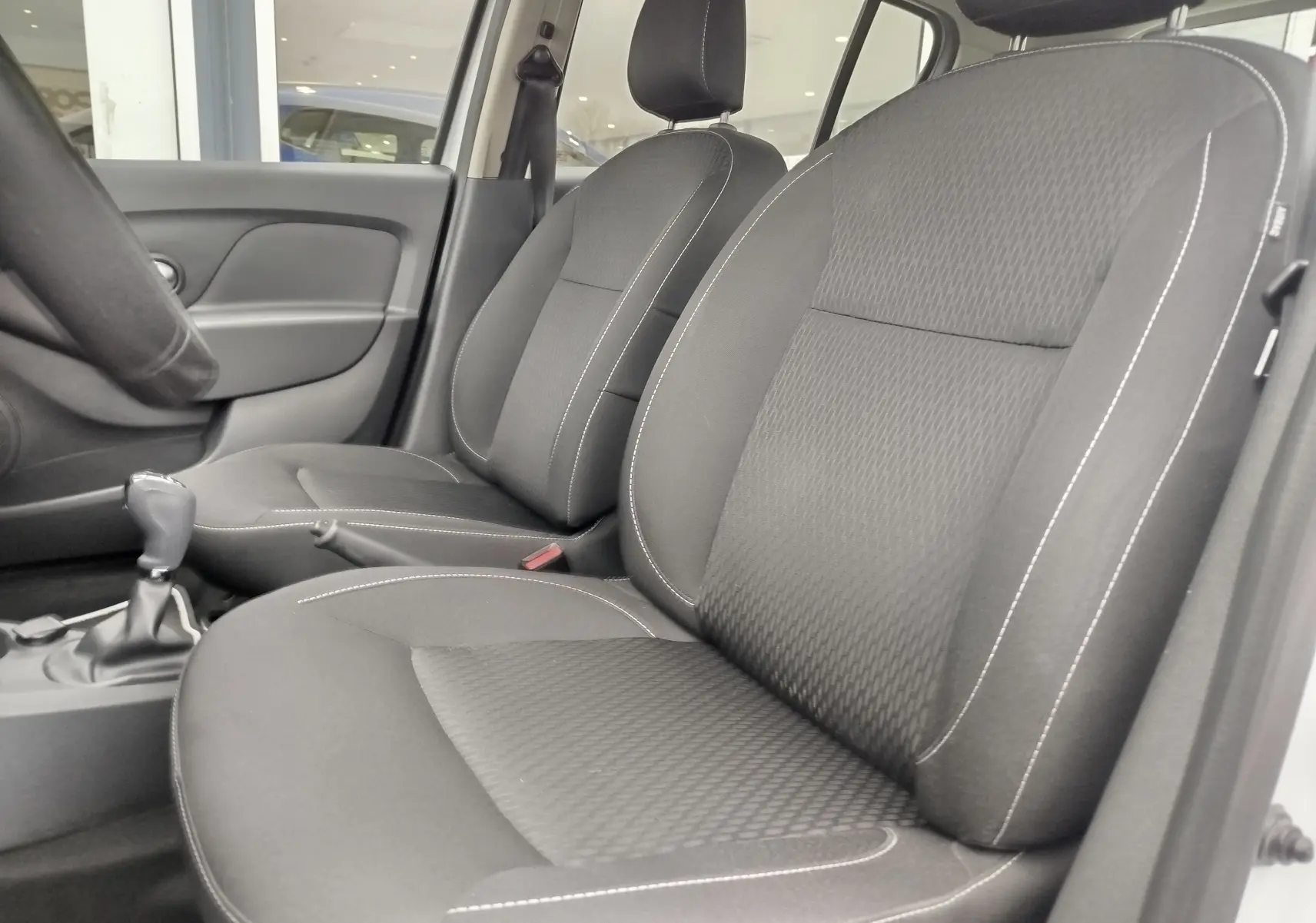 Vue rapprochée des sièges avant en tissu gris foncé avec surpiqûres blanches dans une Dacia Sandero blanc glacier 2019.