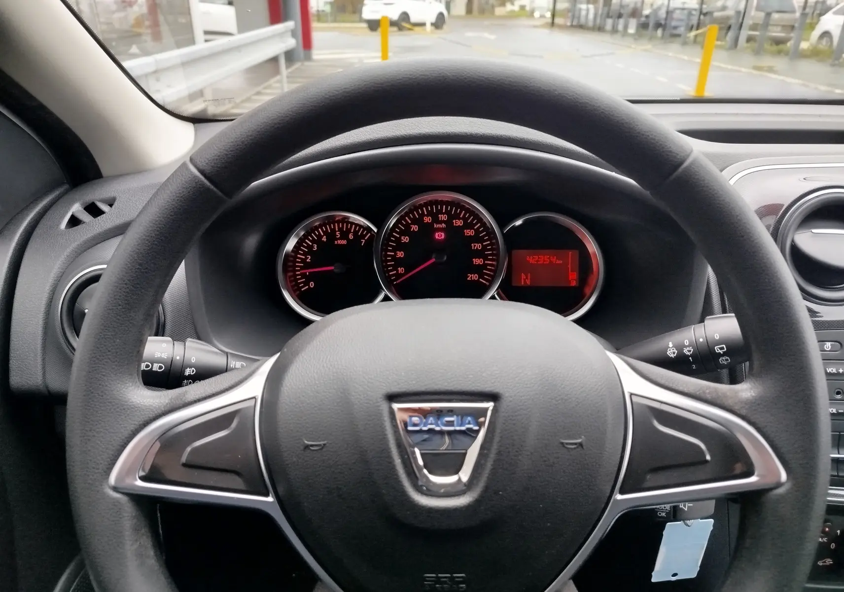 Vue rapprochée du volant et du tableau de bord d'une Dacia Sandero blanche, avec compteurs et indicateurs rouges visibles.