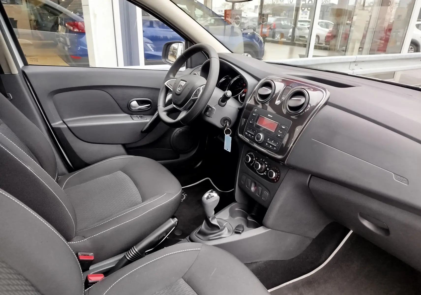 Intérieur avant droit de la Dacia Sandero 2019, sièges tissu gris et tableau de bord avec console centrale noire.