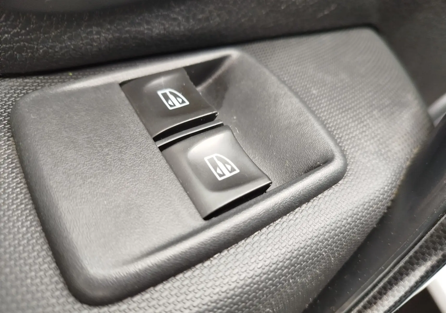 Gros plan sur les boutons de commande des vitres électriques noirs dans l'habitacle d'une Dacia Sandero blanc glacier 2019.