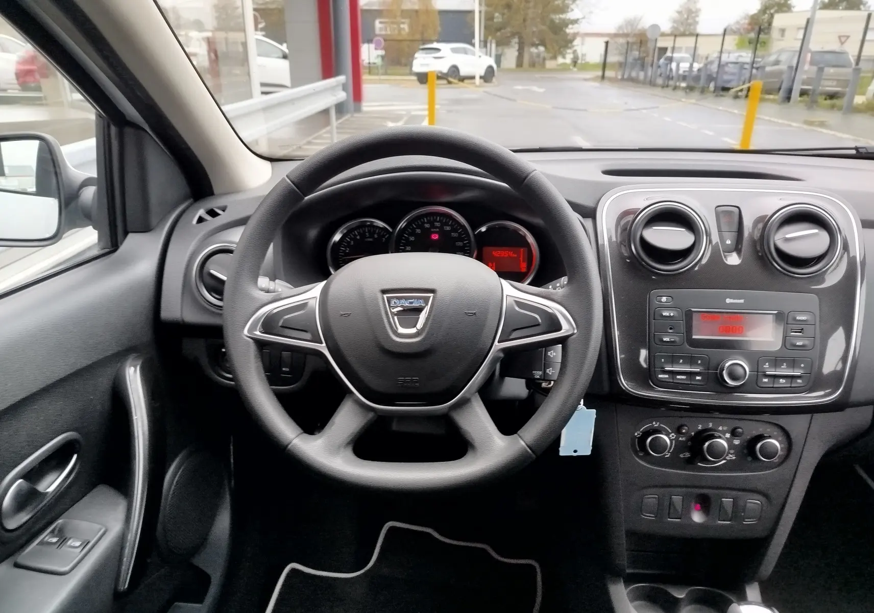 Vue intérieure centrée sur le volant et le tableau de bord noir du Dacia Sandero blanc glacier de 2019.