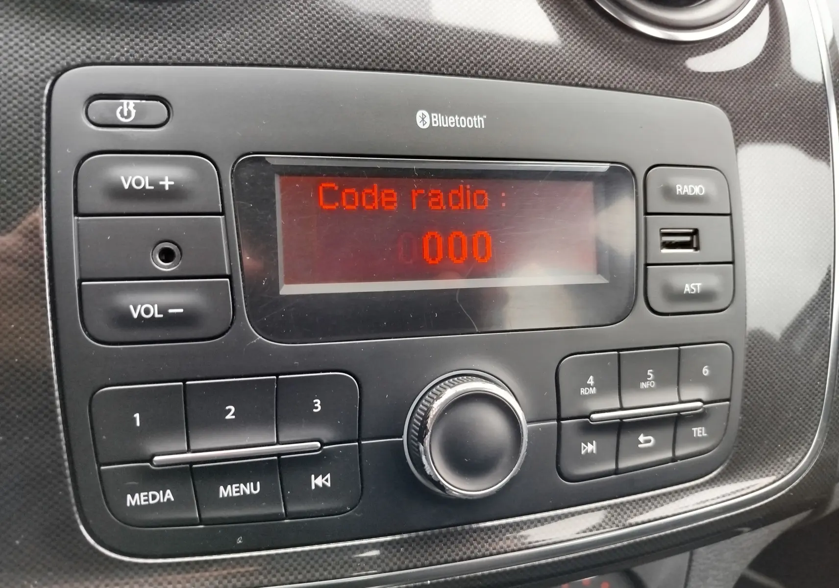 Gros plan sur la radio Bluetooth du tableau de bord d'une Dacia Sandero blanc glacier, affichant "Code radio : 000".
