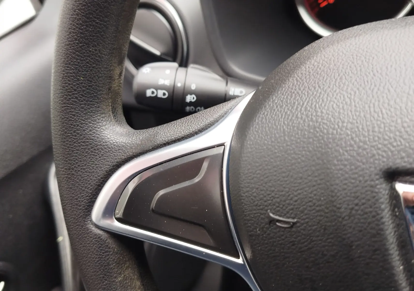 Gros plan sur la partie gauche du volant noir texturé d'une Dacia Sandero blanc glacier, avec commandes intégrées visibles.