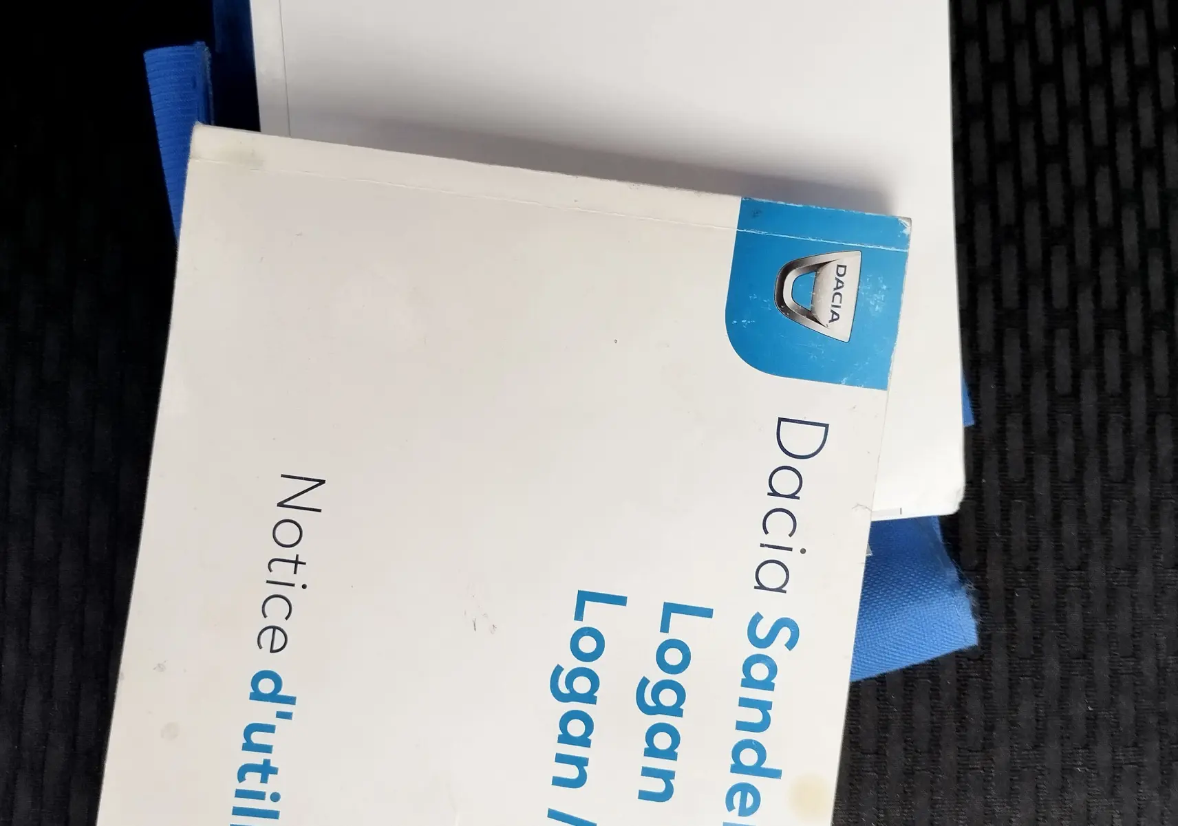 Manuels d'utilisation Dacia Sandero, Logan et Logan MCV posés sur un siège de voiture sombre, vue de dessus.