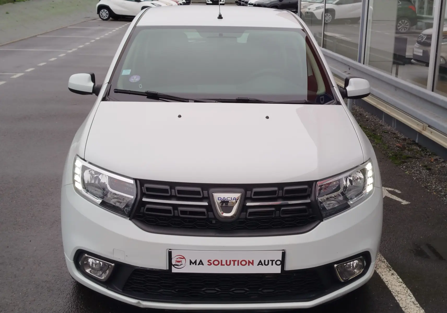 Vue avant d'une Dacia Sandero blanc glacier de 2019 avec phares LED allumés et calandre noire distinctive.