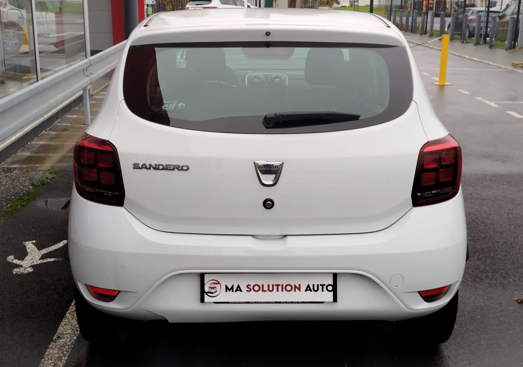 Vue arrière d'une Dacia Sandero blanc glacier de 2019, avec feux arrière sombres et logo centré sur le hayon.