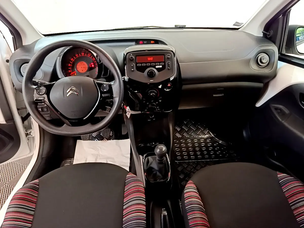 Vue intérieure avant de la Citroën C1 blanche, montrant le tableau de bord, volant et levier de vitesse manuel.