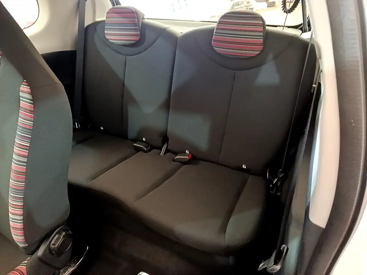 Vue intérieure de la banquette arrière noire avec appuie-têtes rayés rouges et gris de la Citroën C1 blanche.