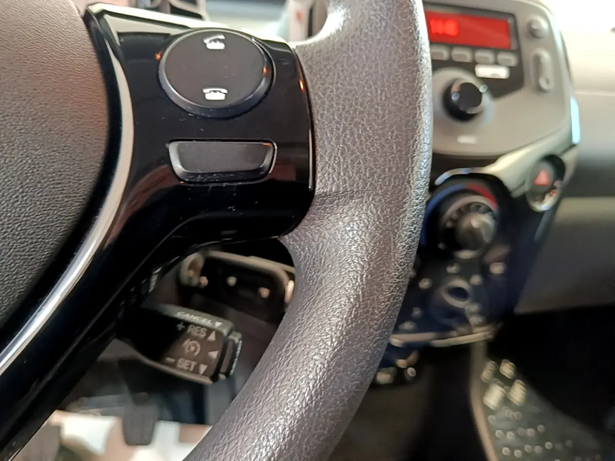 Gros plan sur le volant noir avec commandes intégrées et tableau de bord flou d'une Citroën C1 blanche de 2020.