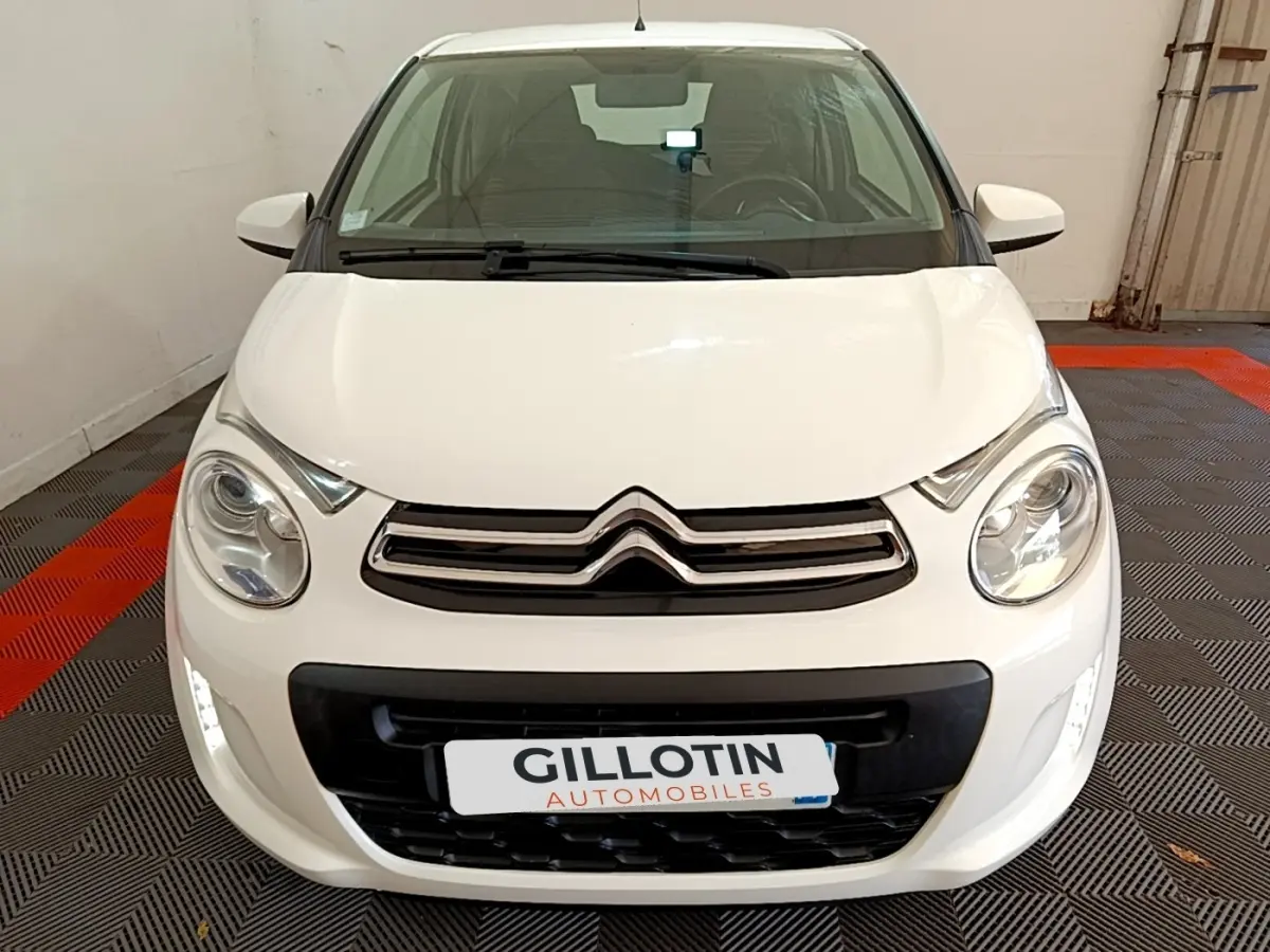 Vue avant d'une Citroën C1 blanche 2020 avec calandre chromée et feux ronds dans un garage.