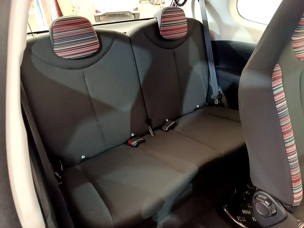 Vue intérieure arrière de la banquette noire avec appuie-têtes rayés rouges et gris de la Citroën C1 blanche.
