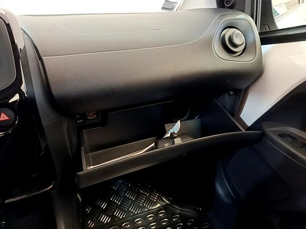 Vue intérieure côté passager de la boîte à gants ouverte sur une Citroën C1 blanche, tableau de bord noir texturé visible.