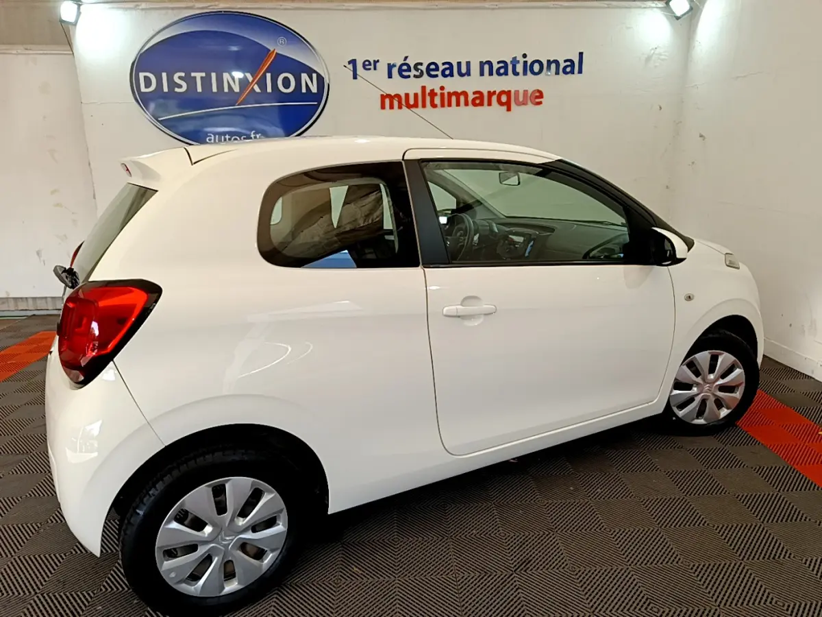 Citroën C1 blanche vue de profil droit en intérieur, avec jantes acier et feux arrière rouges visibles.