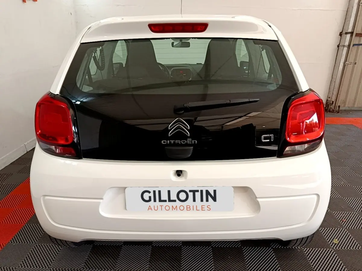 Vue arrière d'une Citroën C1 blanche avec hayon noir brillant et feux arrière rouges dans un garage.