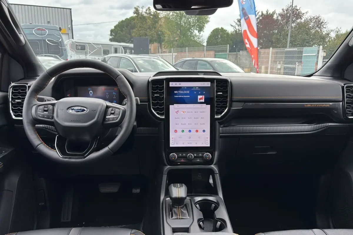 Vue intérieure frontale du Ford Ranger Wildtrak Plus 2025 noir agate, avec écran tactile vertical et volant cuir multifonctions.