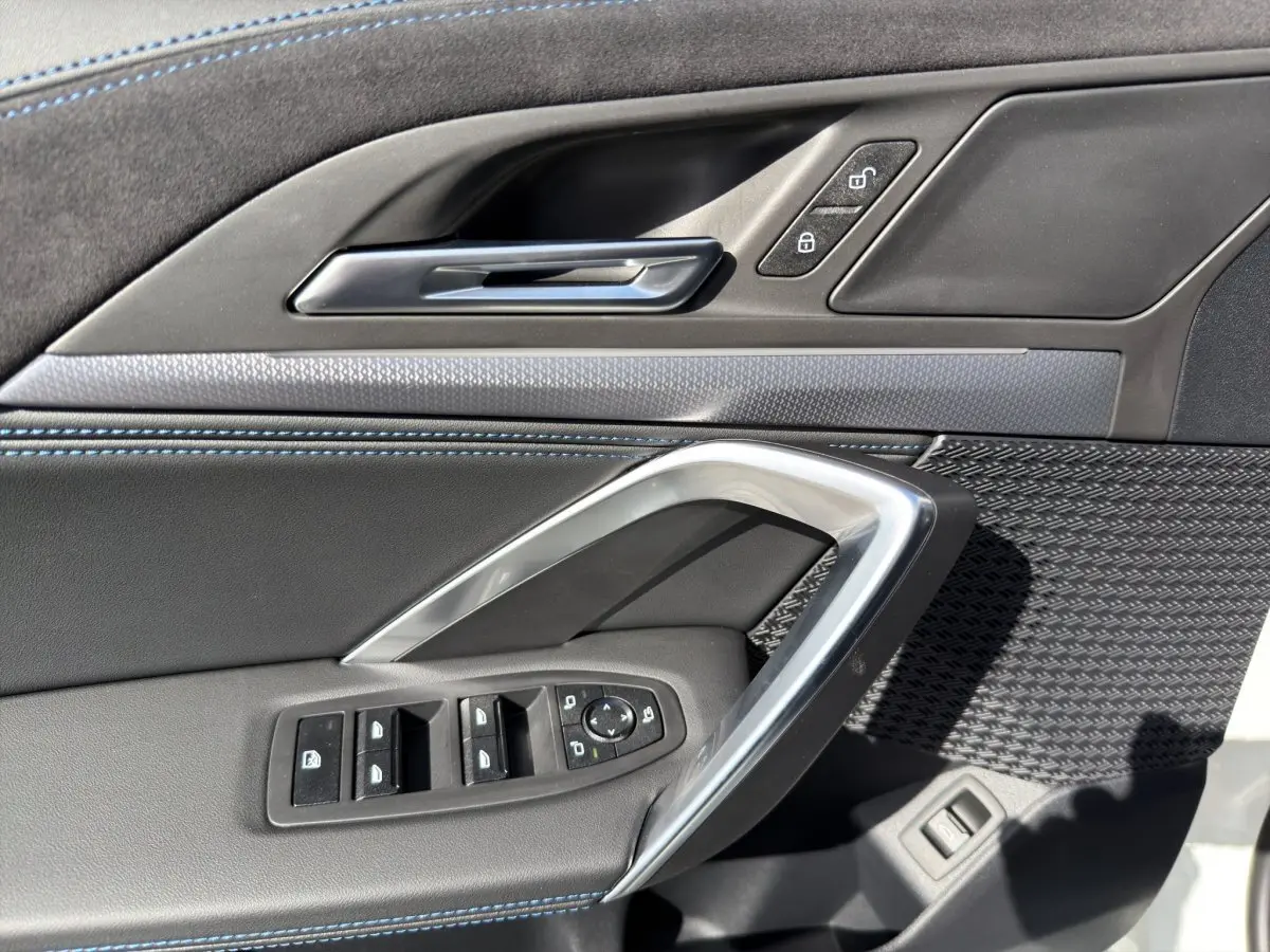 Détail de la porte avant gauche du BMW X1 blanc 2025, avec commandes de vitres et surpiqûres bleues.